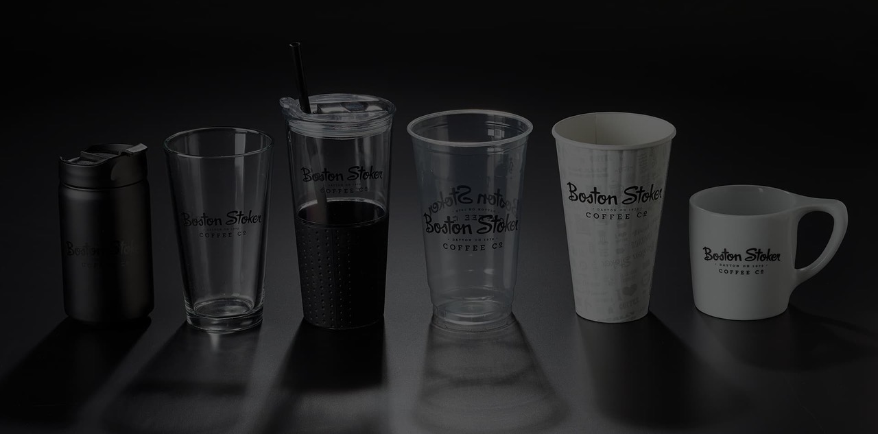 Six coffee vessels in a row carrying the same imprinted logo: insulated travel tumbler, pint glass, lidded cold cup with straw, clear plastic cup, paper hot cup and ceramic mug