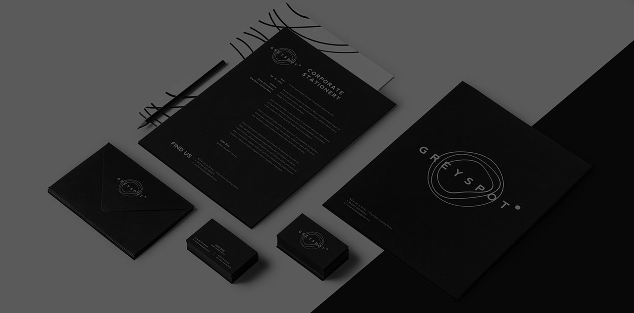 Matte black stationery suite arranged on grey: letterhead, envelope, two stacks of business cards, pencils and a large logo presentation board